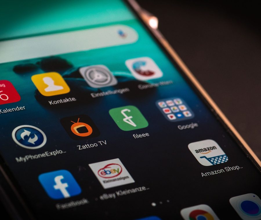 完美对战平台 App 主界面在手机屏幕上展开，深绿色房间列表与实时延迟曲线上方浮着半透明数据面板，桌面台灯在旁投下暖光，整体是深夜开黑前的气氛